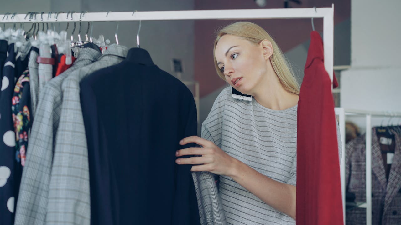 services-img Woman browsing clothes while talking on phone in a store. Multitasking and fashion concept.